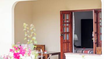 An open wooden door leading to a room with a bed, a bedside table, and a lamp.