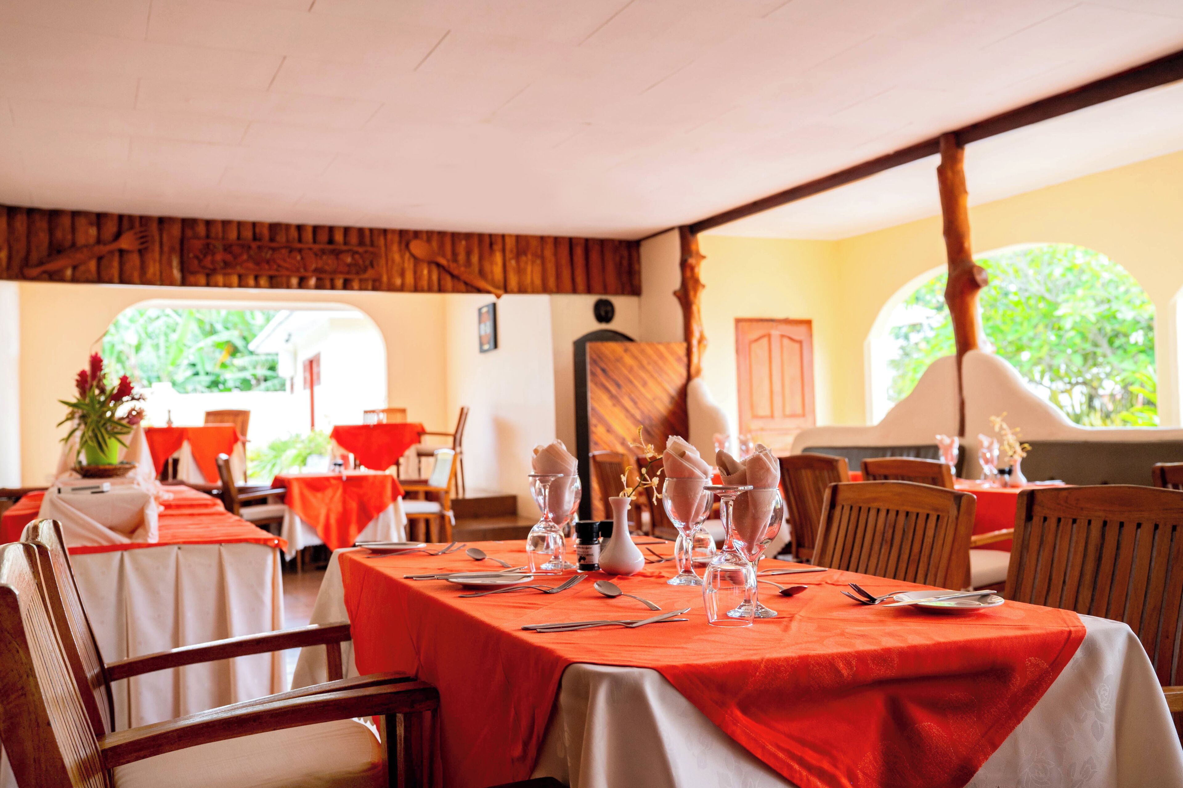 Ein Restaurant mit gedeckten Tischen, Holzsesseln und Blick auf eine grüne Umgebung.