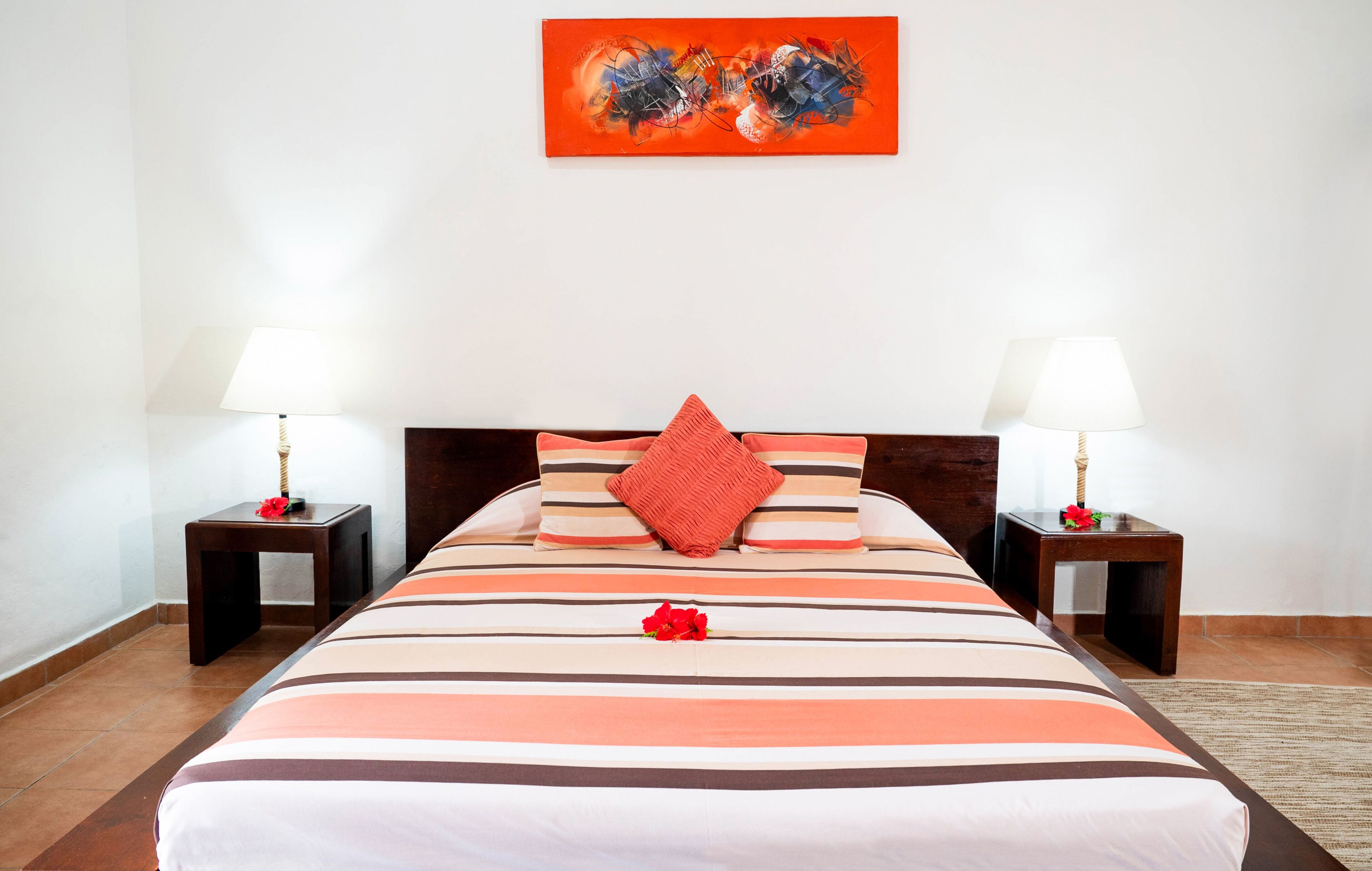 A hotel room with a large bed, two bedside tables with lamps, a red pillow, and a painting on the wall.