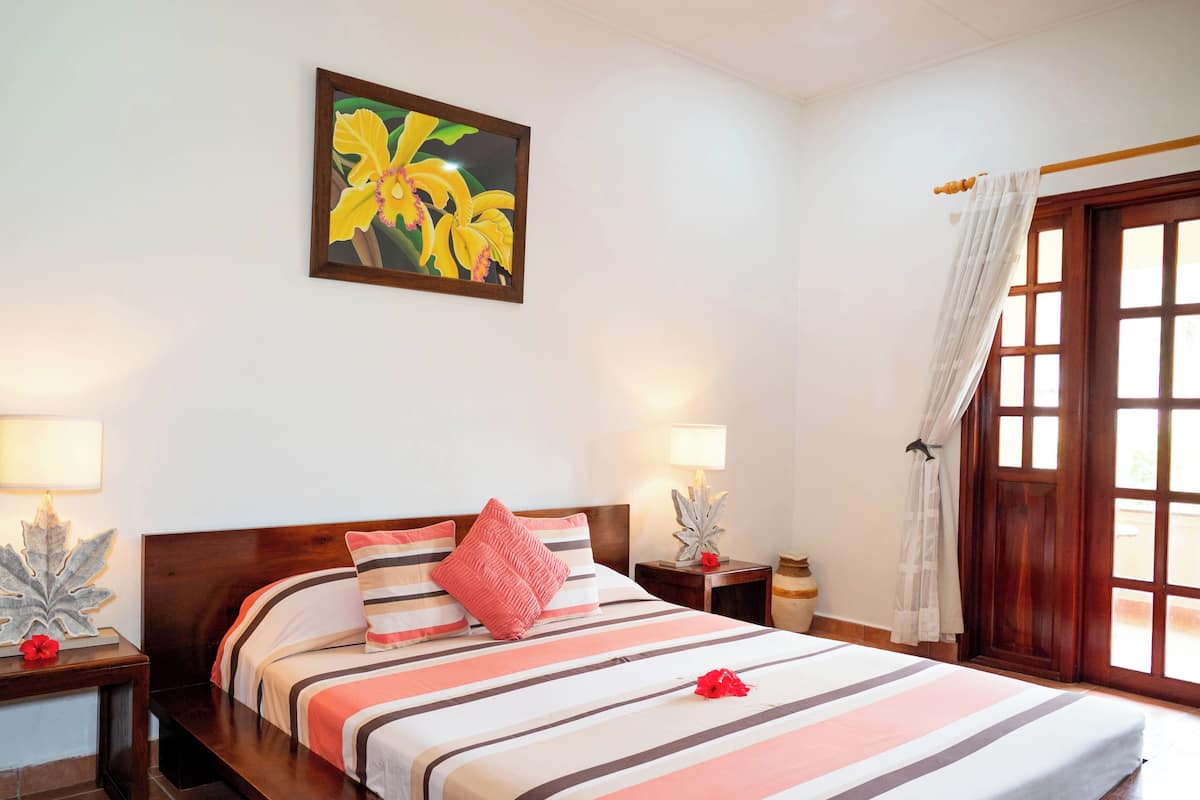 Habitación de hotel con una cama, dos mesitas de noche, una lámpara de noche, un ventanal con cortinas y un cuadro colgado en la pared.