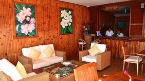 Zona de recepción con paneles de madera, un mostrador de recepción y arreglos de asientos que incluyen un sofá y sillas.