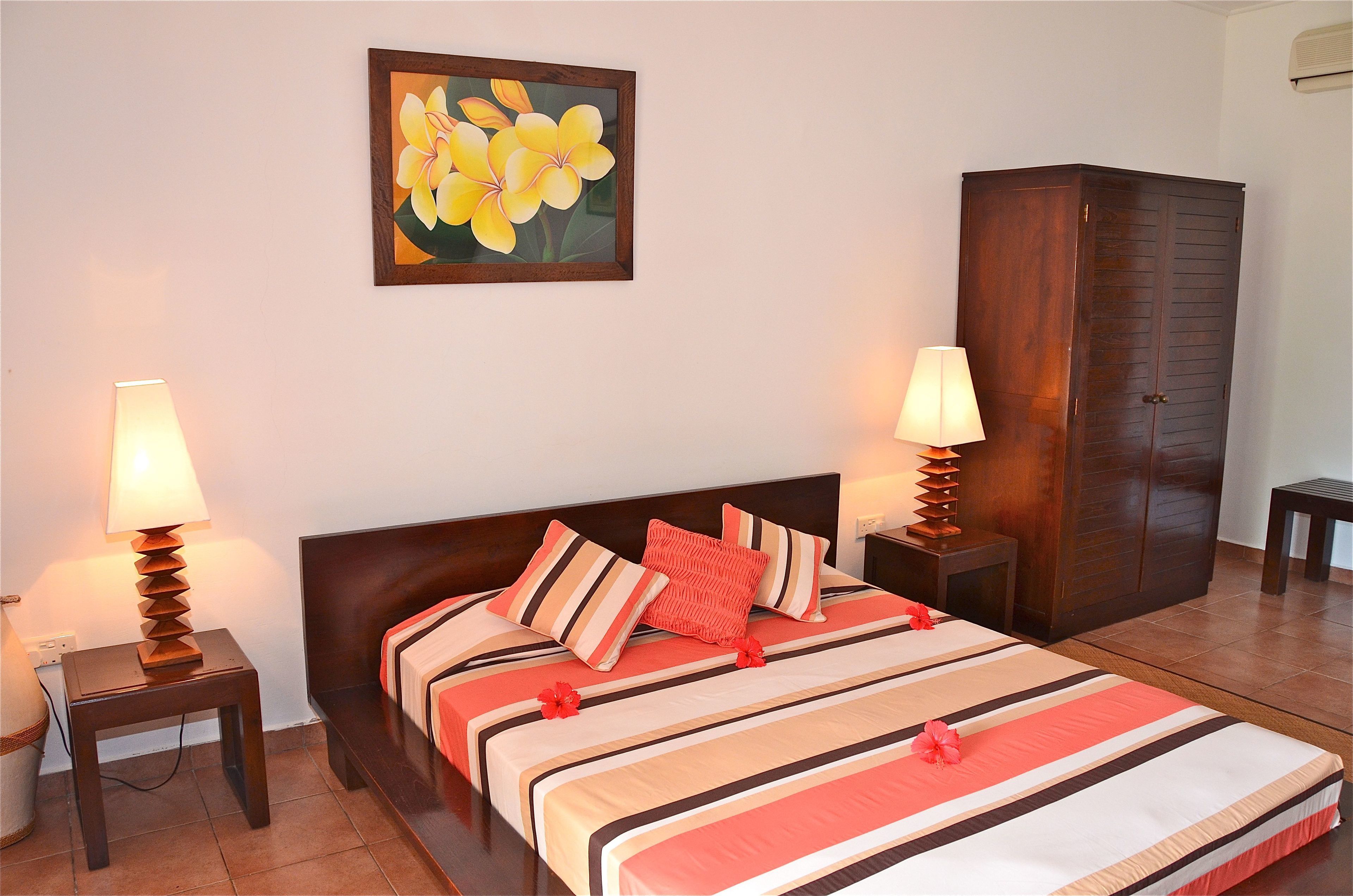 Ein Hotelzimmer mit einem großen Bett, zwei Nachttischen mit Lampen, einem Kleiderschrank und einem floralen Gemälde an der Wand.