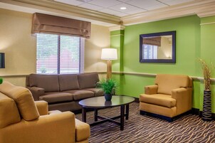 A hotel room with a brown sofa, a beige armchair, a small round table, and a green accent wall.
