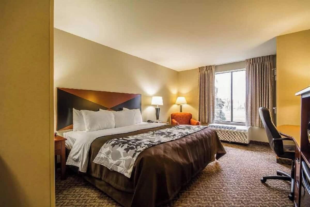 Camera d'albergo con un letto, due lampade sui comodini, una sedia, una scrivania e una finestra con tende.