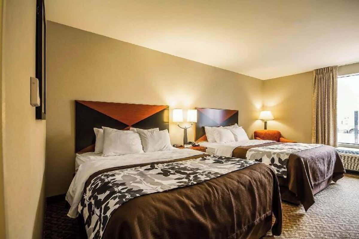Camera d'albergo con due letti, un'ampia finestra con tende e una lampada fissata alla parete.