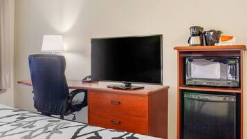 A hotel room with a bed, a desk with a computer, a chair, a lamp, a microwave, and a coffee maker.