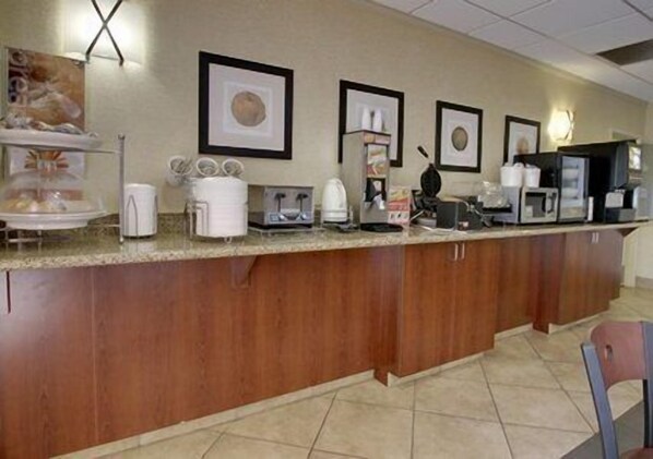 A hotel breakfast area with a long counter, coffee makers, a microwave, and framed pictures on the wall.