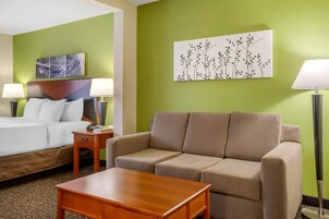 A hotel room with a bed, a sofa, a wooden table, and two wall-mounted lamps.