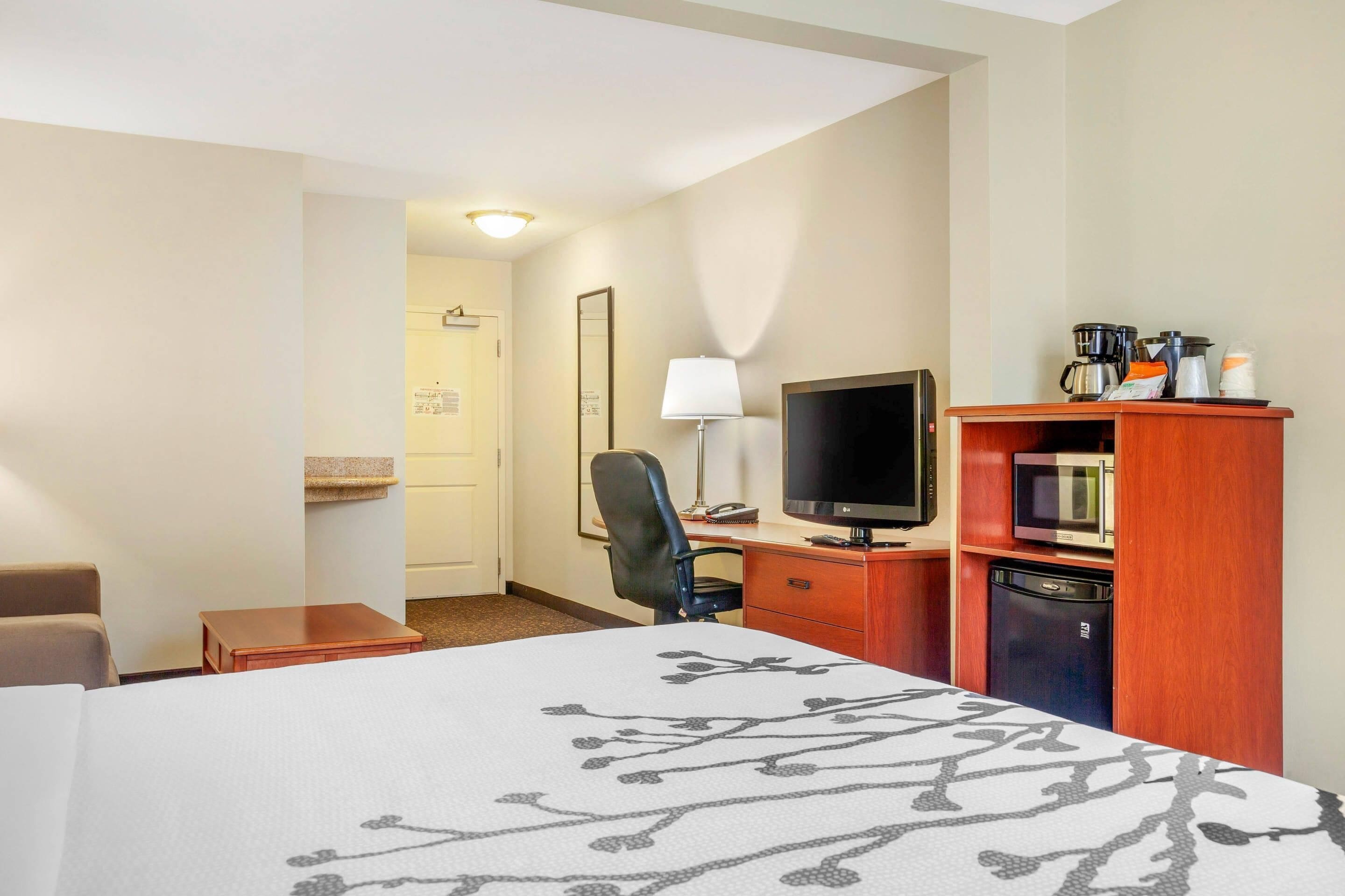 A hotel room with a bed, a desk with a computer, a TV, a coffee maker, and a microwave.