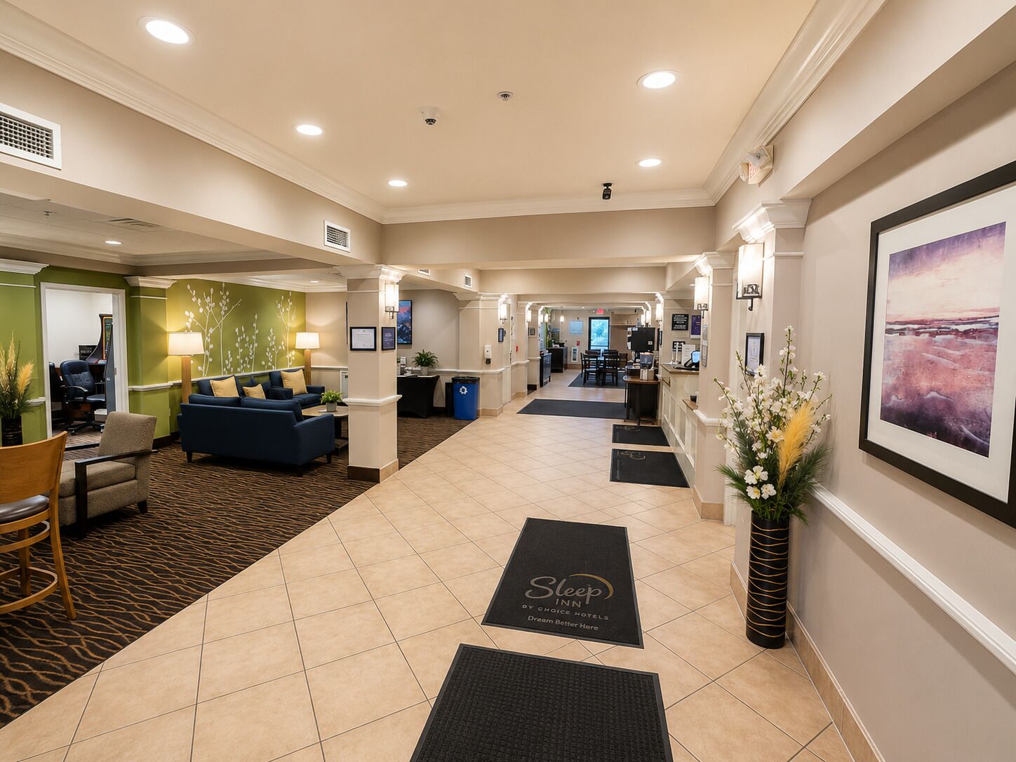 A hotel lobby with a reception desk, seating area, and a large framed artwork on the wall.
