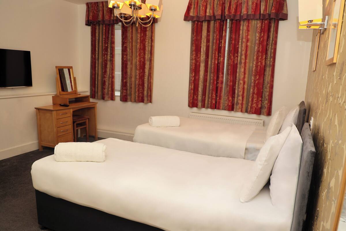 Habitación de hotel con dos camas, un escritorio, una silla, un televisor y una ventana con cortinas.