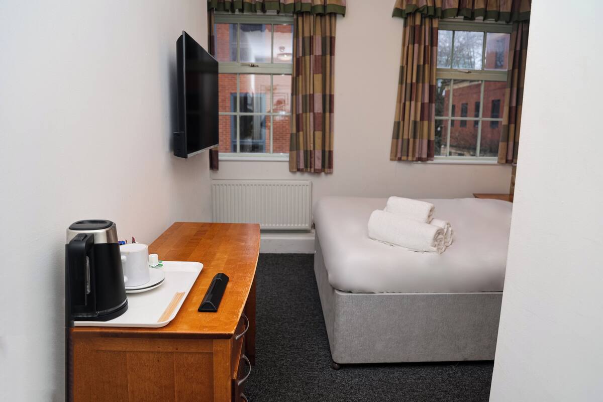 Una habitación de hotel con una cama, un escritorio con cafetera, un control remoto y un televisor en la pared.