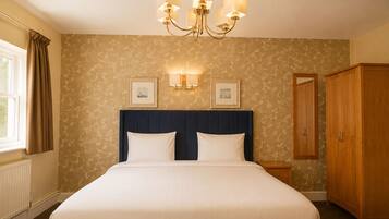 Quarto de hotel com uma cama grande, um candelabro, um guarda-roupa e uma janela com cortinas.