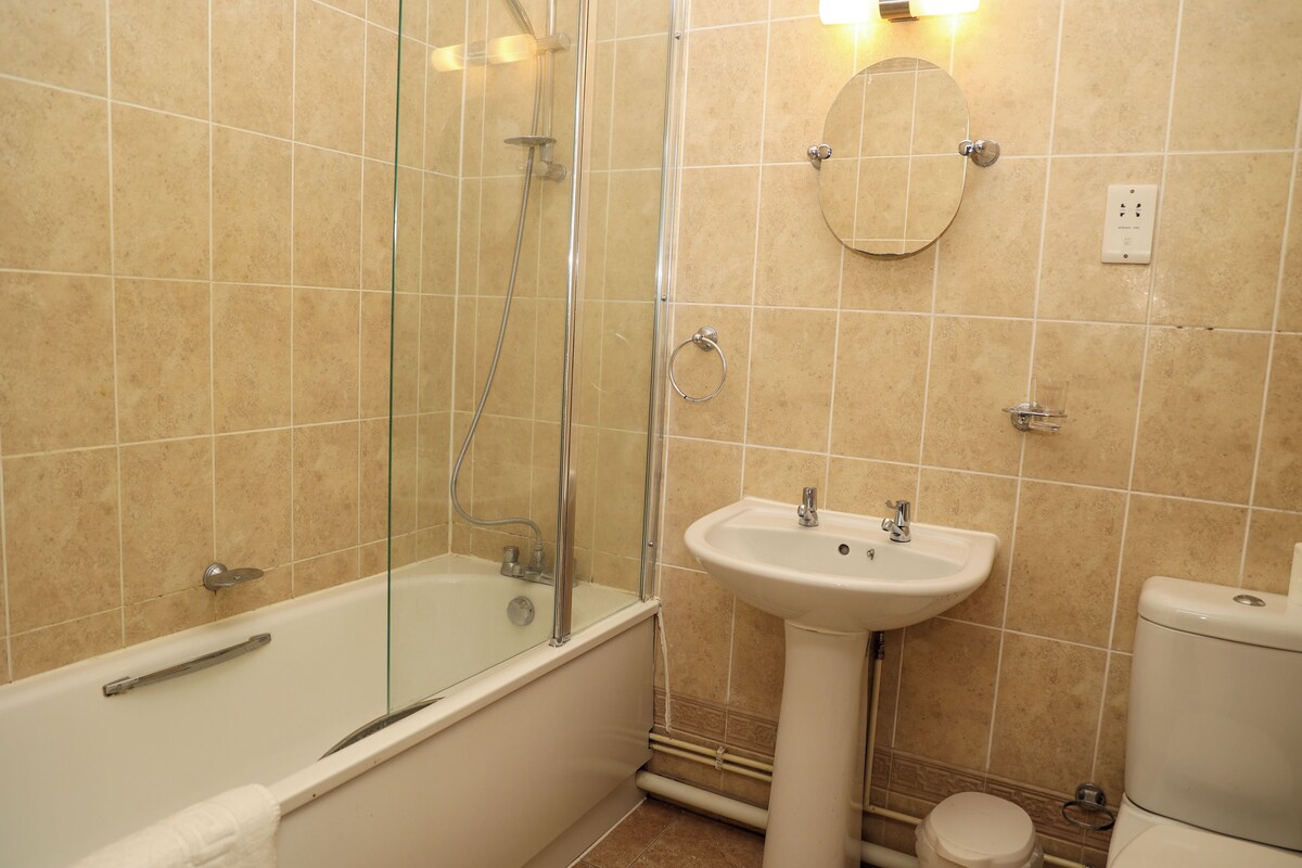 Un baño con ducha de vidrio, bañera blanca, lavamanos pedestal y retrete.