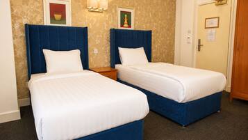 Habitación de hotel con dos camas, una mesita de noche, una lámpara de pared y una puerta con un letrero.