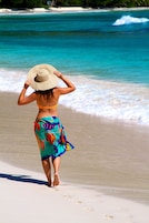 Una persona caminando sobre la playa con sombrero.