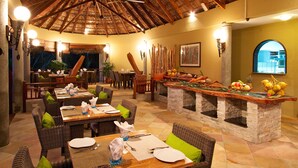 Un restaurante con mesas y sillas de madera, techo de paja y barra de piedra.