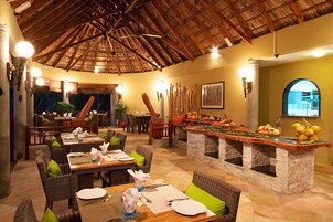 Un restaurante con mesas y sillas de madera, techo de paja y barra de piedra.