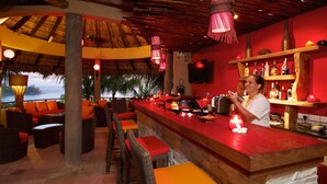 Zona de bar con mobiliario de mimbre, una barra roja y vistas al océano.