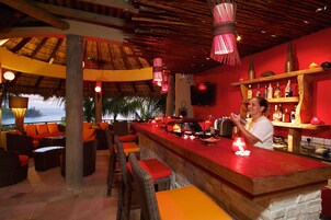 Zona de bar con mobiliario de mimbre, una barra roja y vistas al océano.