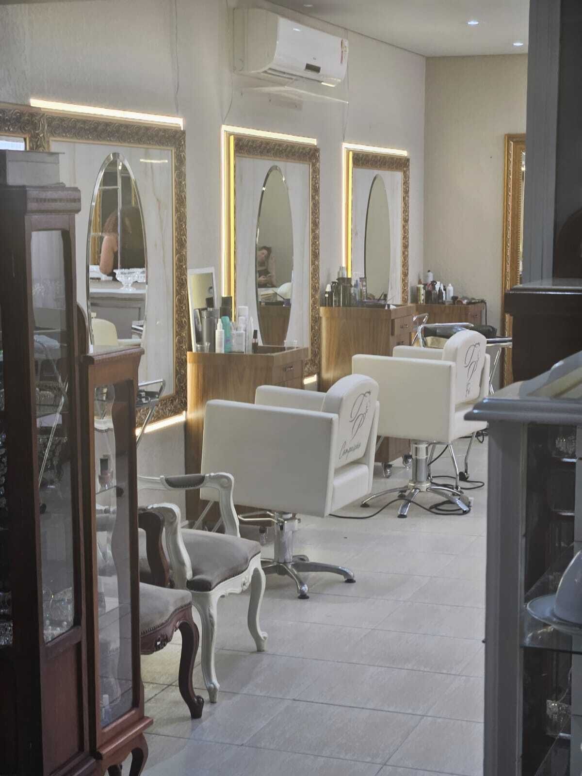 A salon with three white salon chairs, a wooden vanity, and large mirrors with gold frames.