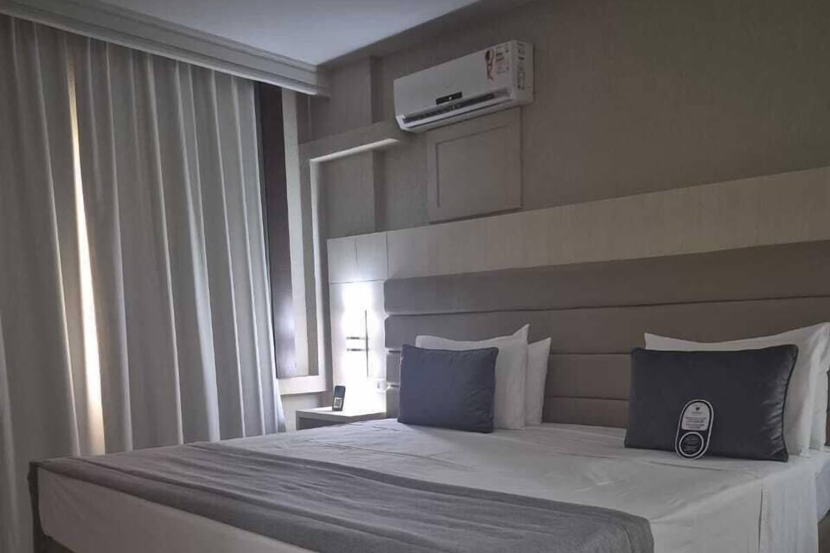 A modern hotel room with a large bed, a nightstand, and an air conditioning unit on the wall.