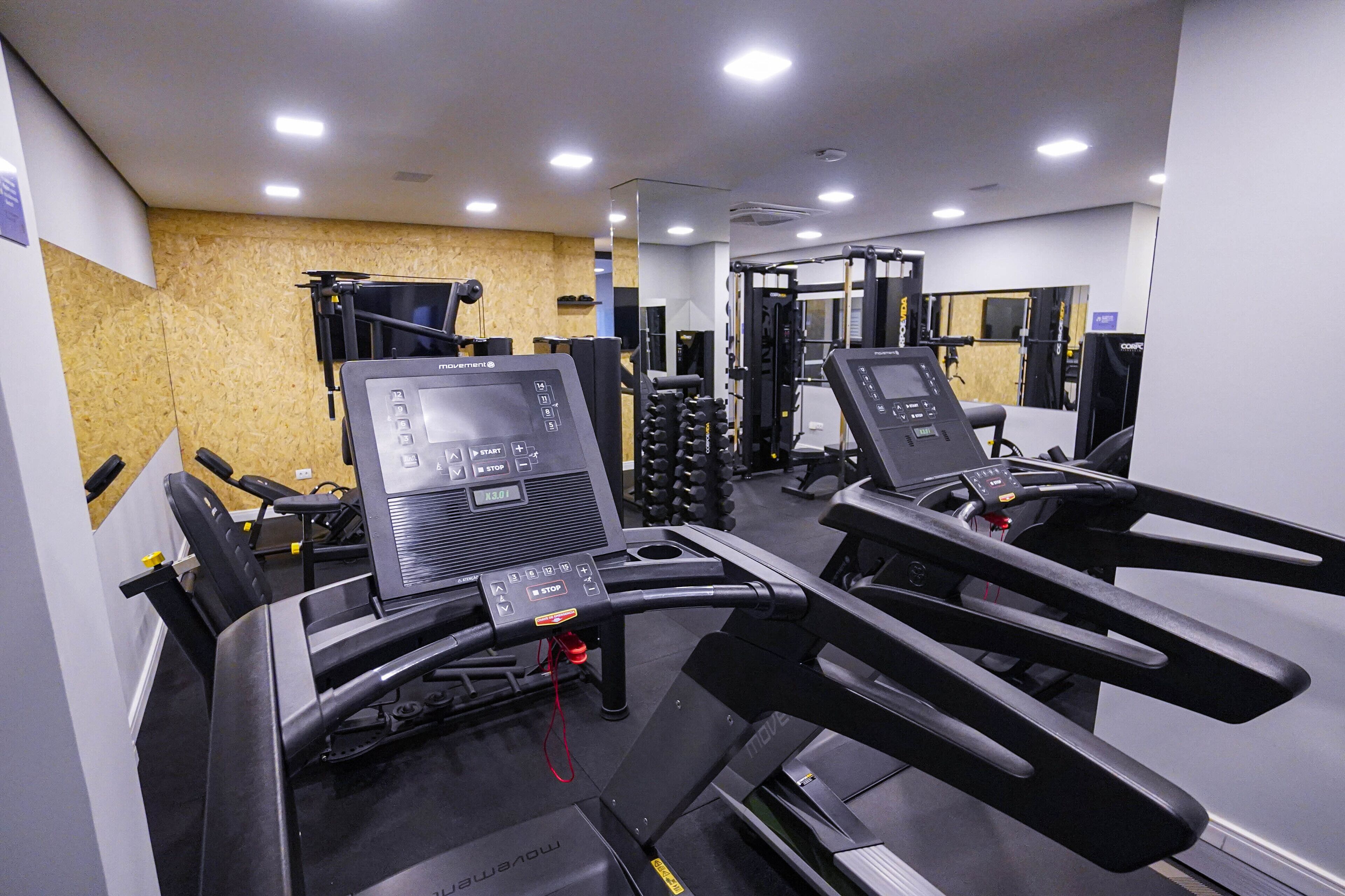 Ett gym med löpband, styrketräningsmaskiner och en vägg täckt med speglar.