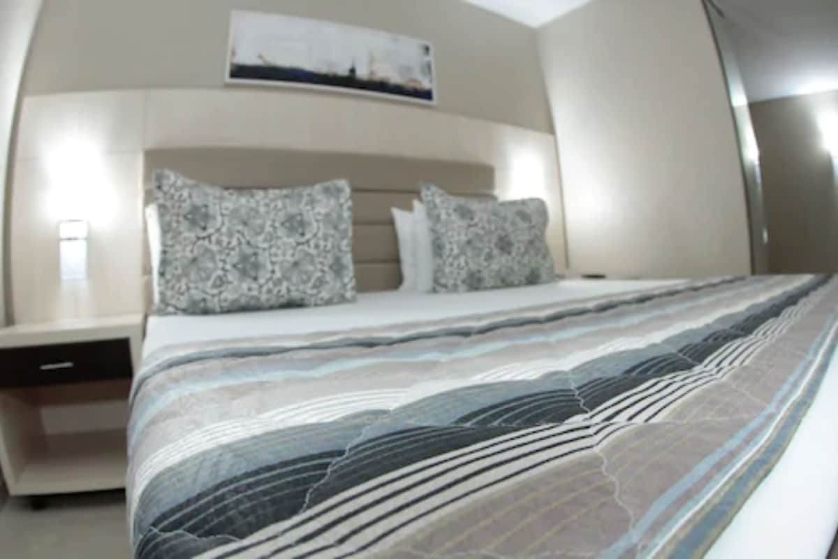 A bedroom with a bed, pillows, a nightstand, and a wall-mounted artwork.