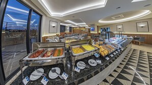 A buffet area with various food stations, a seating area with tables and chairs, and a large window offering a view of the sky. - Hotel Metrópole Maringá (Maringá)