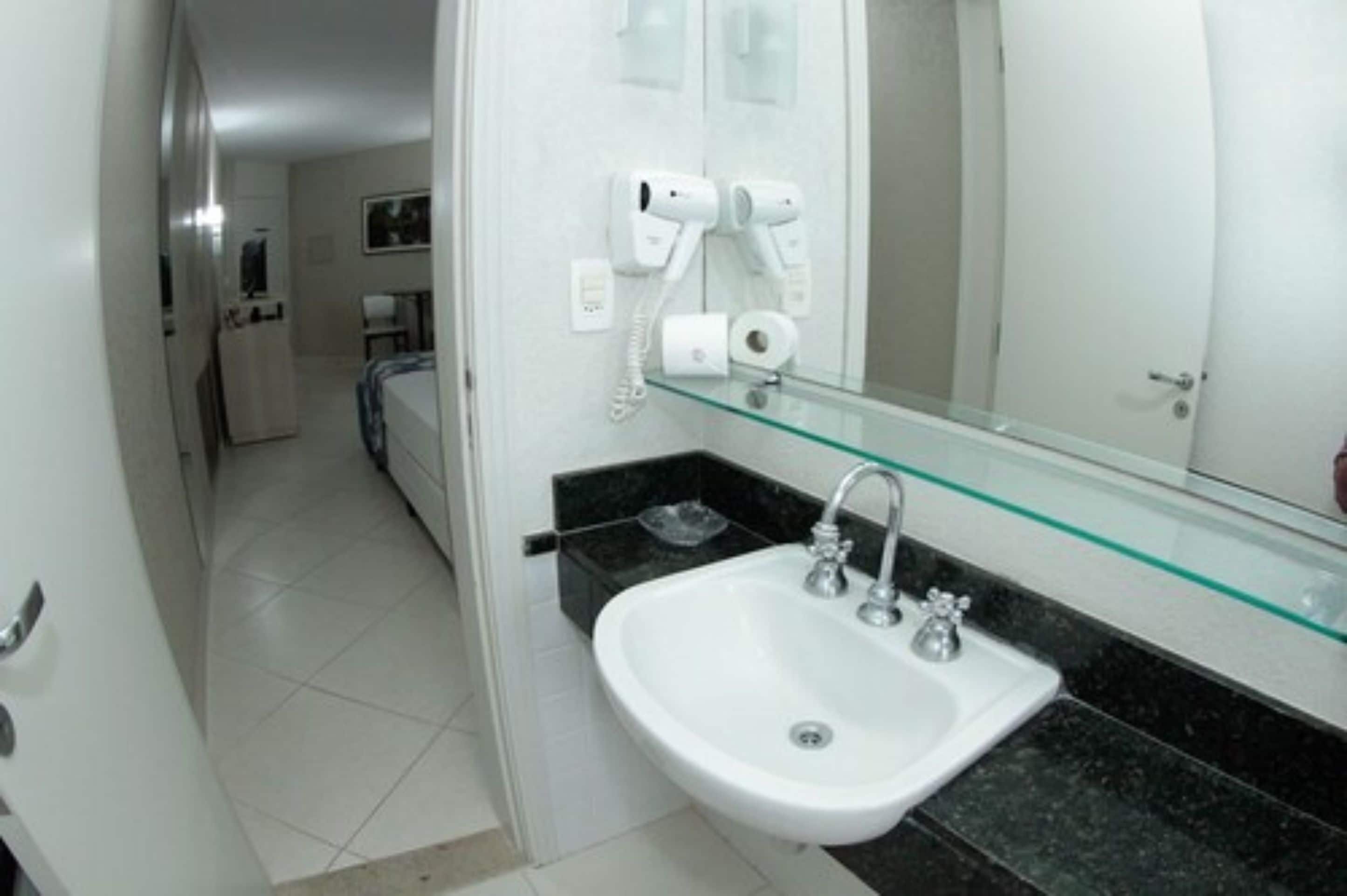 Un baño con un lavamanos blanco, un estante de vidrio y un espejo.