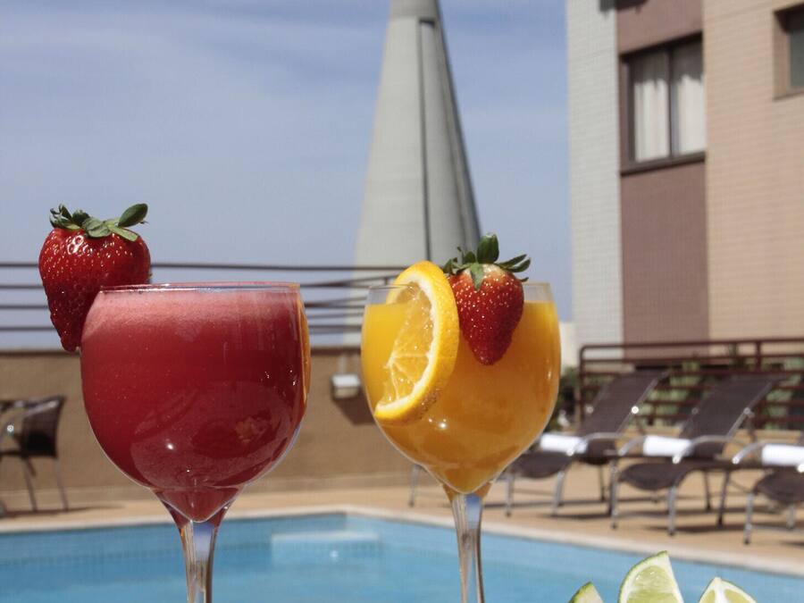 Una mesa junto a la piscina con dos bebidas, un plato de queso, aceitunas y una fuente de jamón.
