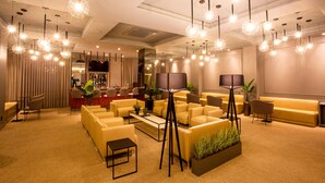 A modern hotel lobby with sofas, a bar area, and pendant lighting. - Hotel Metrópole Maringá (Maringá)