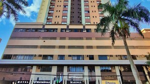 A tall hotel building with multiple floors, a central entrance, and a surrounding landscaped area with palm trees. - Hotel Metrópole Maringá (Maringá)