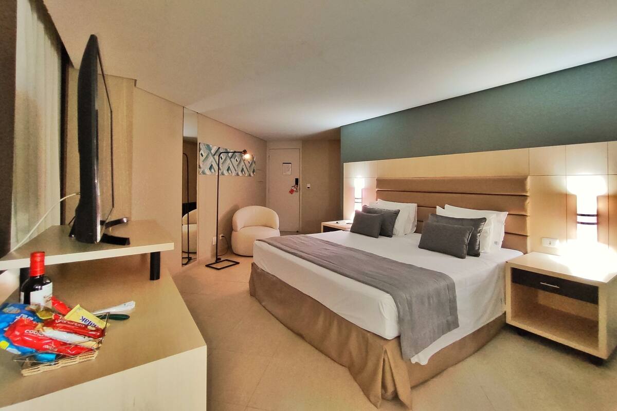A hotel room with a bed, bedside tables, a desk, a chair, a TV, and a mirror.
