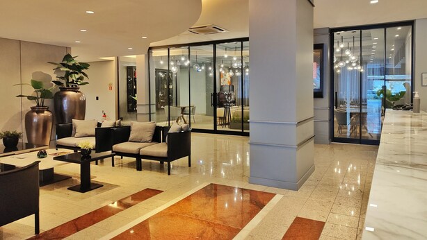 A modern hotel lobby with seating areas, a reception desk, and a glass partition separating the lobby from the dining area. - Hotel Metrópole Maringá (Maringá)
