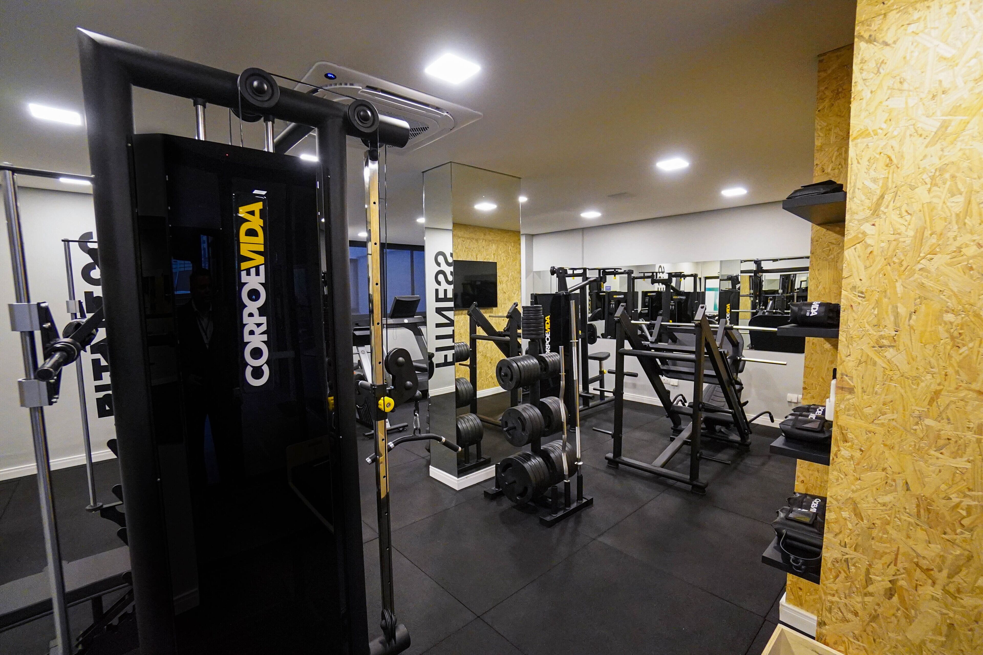 A gym with various weightlifting equipment, mirrors, and a wooden accent wall.