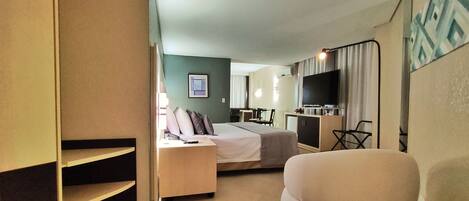 A hotel room with a bed, a desk, a chair, a TV, and a dining area.