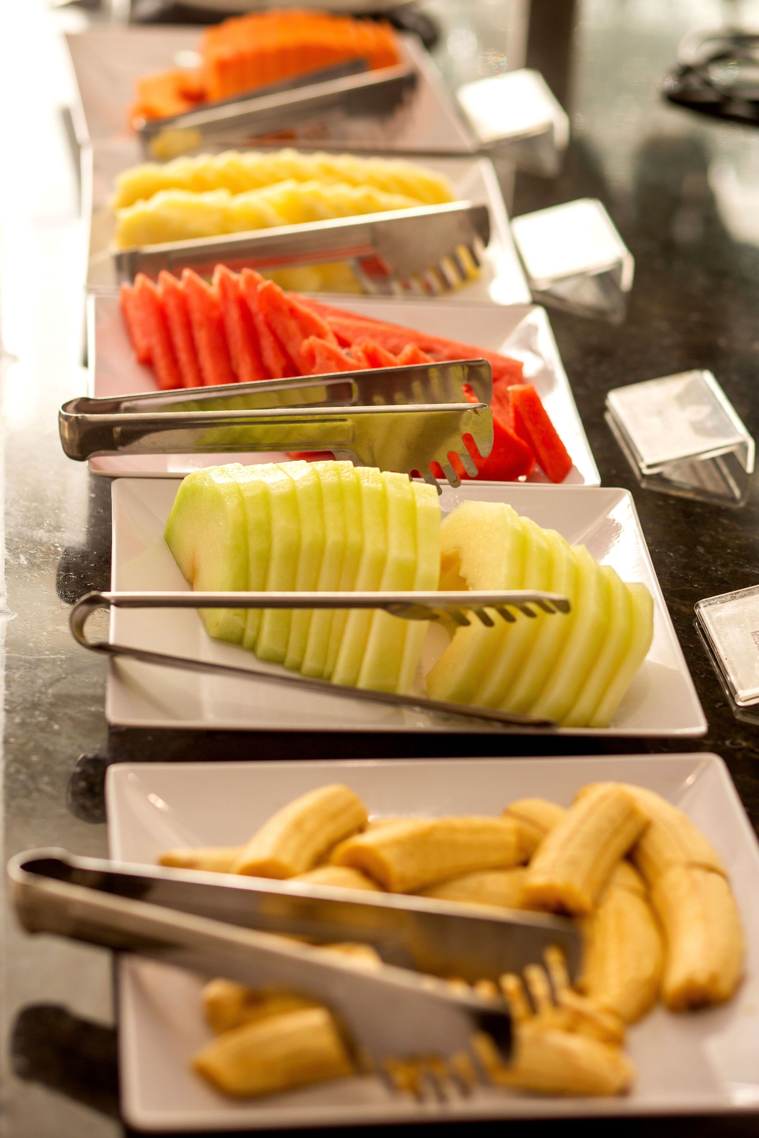 A buffet with various fruits and vegetables, including sliced apples and carrots, arranged on white plates.