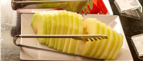 Un bufé con diversas frutas y verduras, entre ellas manzanas y zanahorias en rodajas, dispuestas sobre platos blancos.