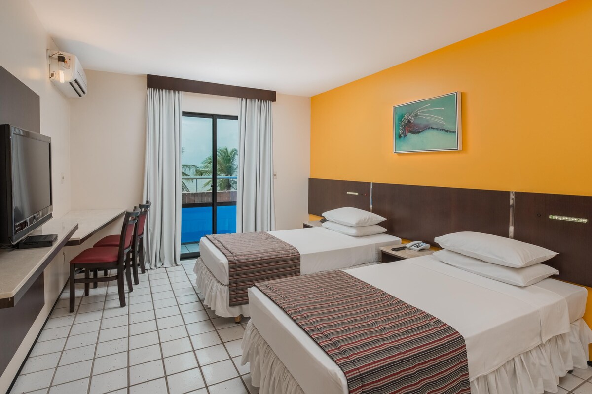 Une chambre d’hôtel avec deux lits, un bureau avec une télévision et un balcon avec des rideaux.
