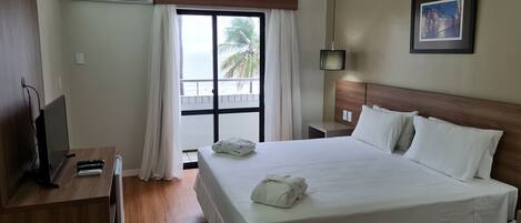 Habitación de hotel con cama, televisión, escritorio y ventana con cortinas.