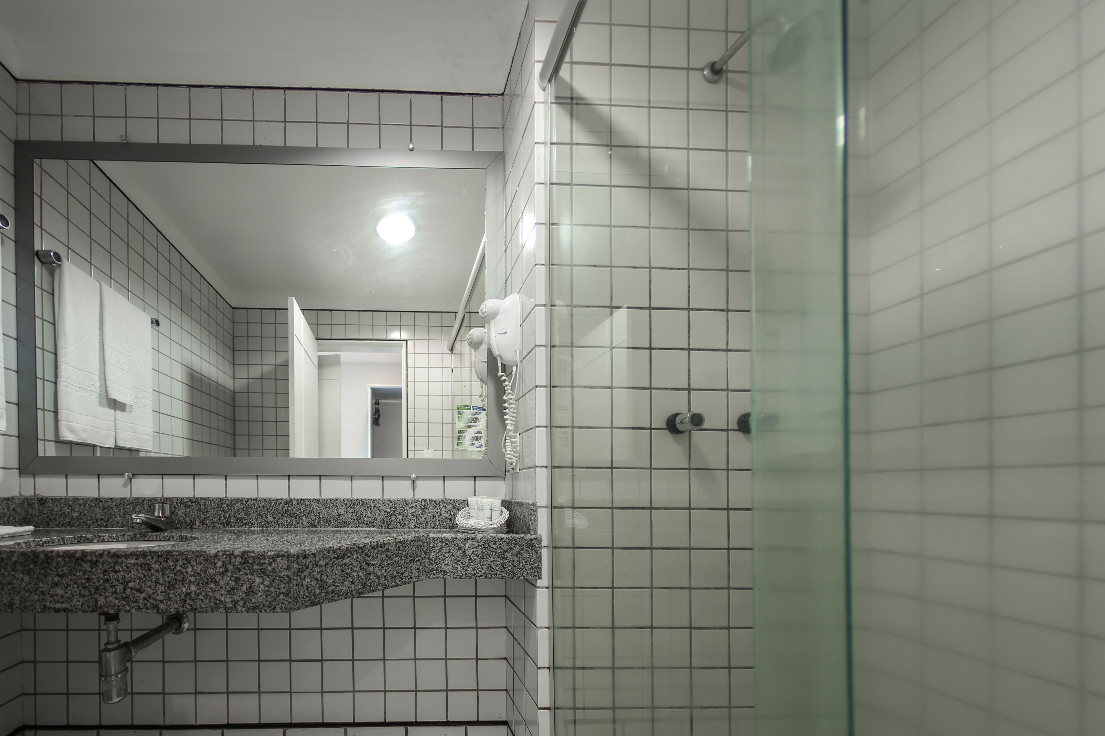 A bathroom with a granite countertop, a glass shower enclosure, and white tiled walls.