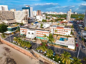A coastal cityscape with a prominent hotel featuring multiple floors, a rooftop pool, and a beachfront location. - Brisamar Hotel & SPA São Luís (São Luís)