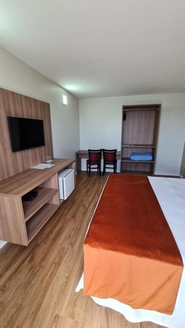 A hotel room with a wooden desk, a television, a bed with a brown cover, two chairs, and a wardrobe. - Brisamar Hotel & SPA São Luís (São Luís)