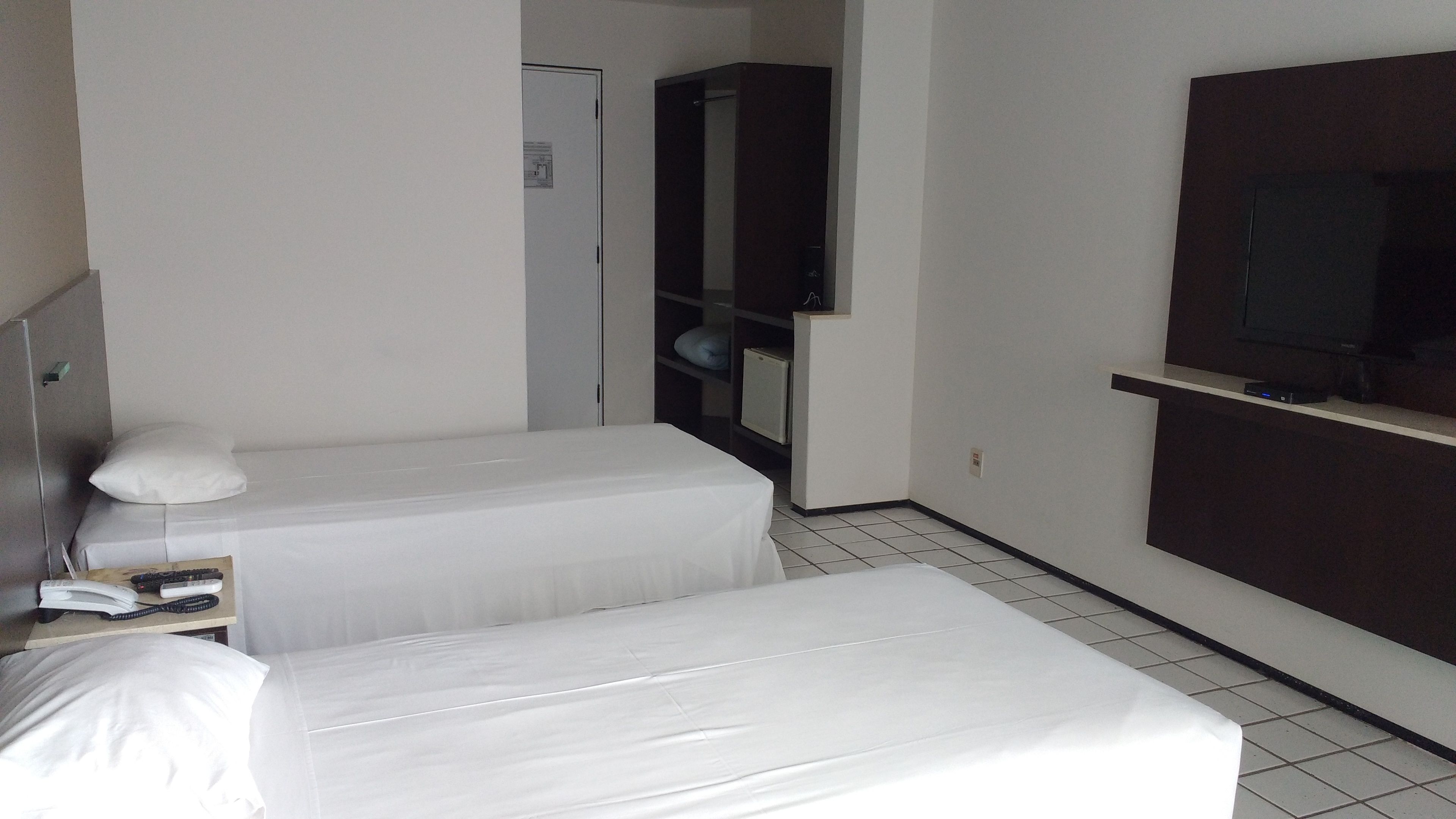 A hotel room with two single beds, a small desk with a telephone, and a TV mounted on the wall.
