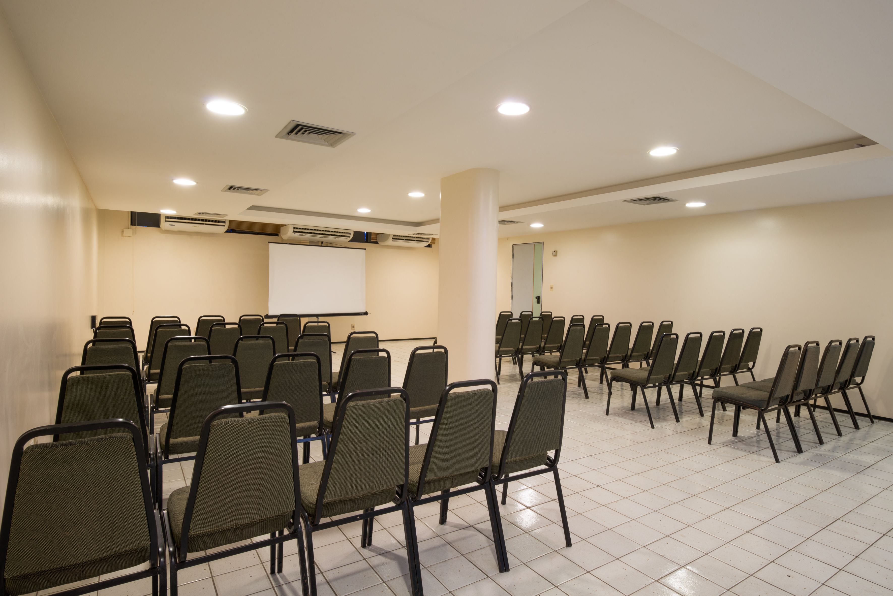 A conference room with rows of chairs, a whiteboard, and air conditioning units.