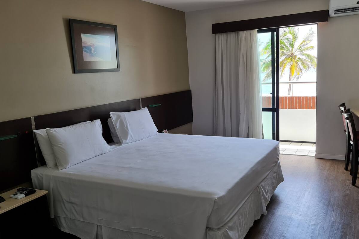 A hotel room with a large bed, a desk with a chair, a television, and a window with curtains.