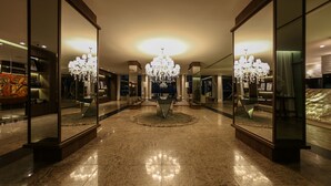 Een ruime lobby met een centrale kroonluchter, spiegelende wanden en een gepolijste marmeren vloer.