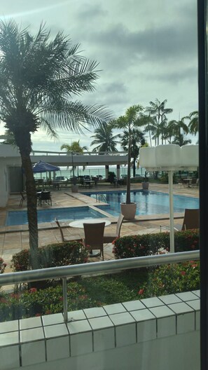 A pool area with lounge chairs, a palm tree, and a view of the ocean. - Brisamar Hotel & SPA São Luís (São Luís)