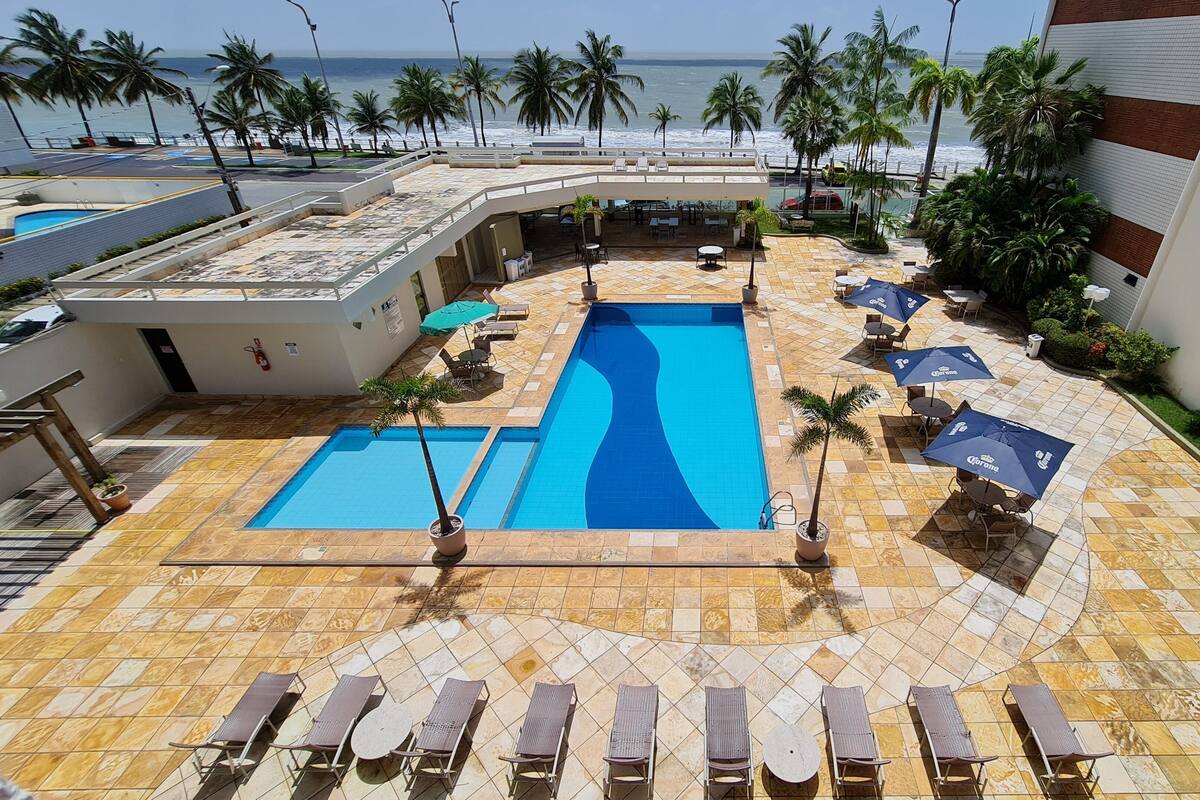 A rooftop pool area with two swimming pools, lounge chairs, and umbrellas.